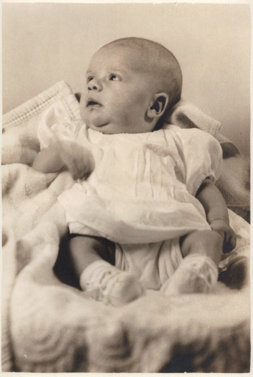 Infant in white dress against plain background.