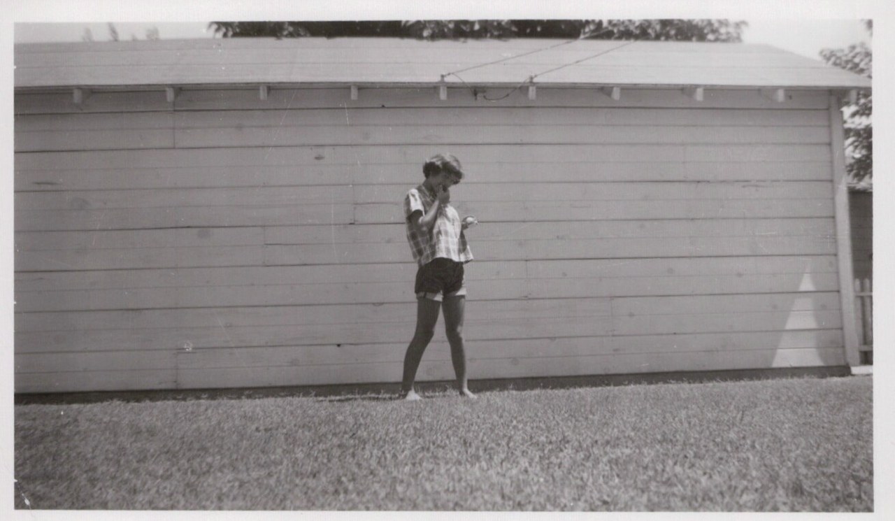 Child standing in front of garage with lawn.
