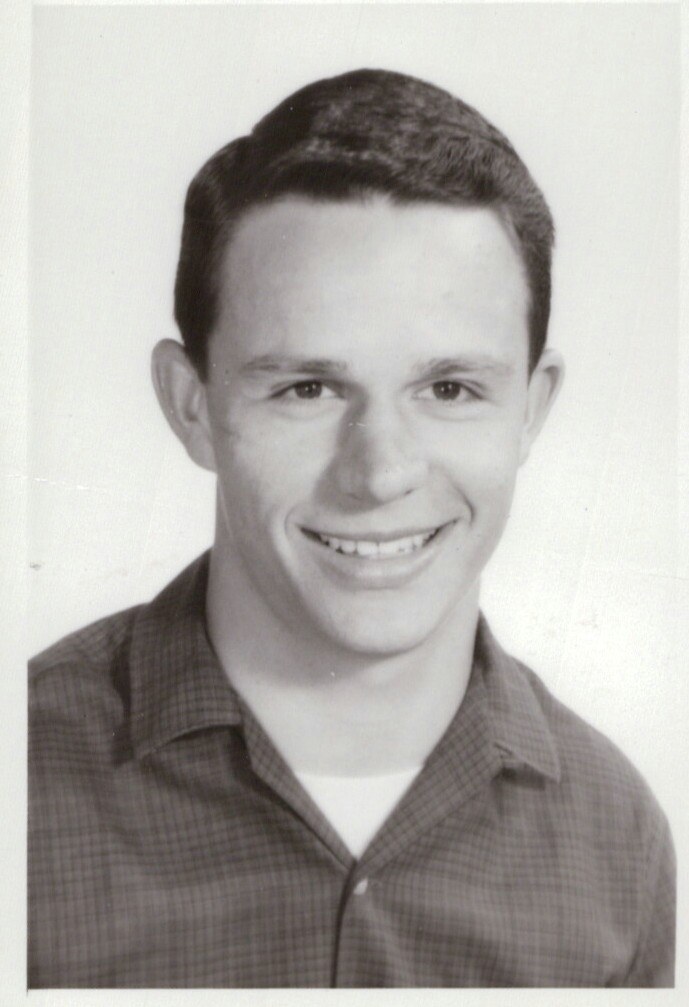 Head-and-shoulders portrait of a smiling young man in a collared shirt against a plain background.