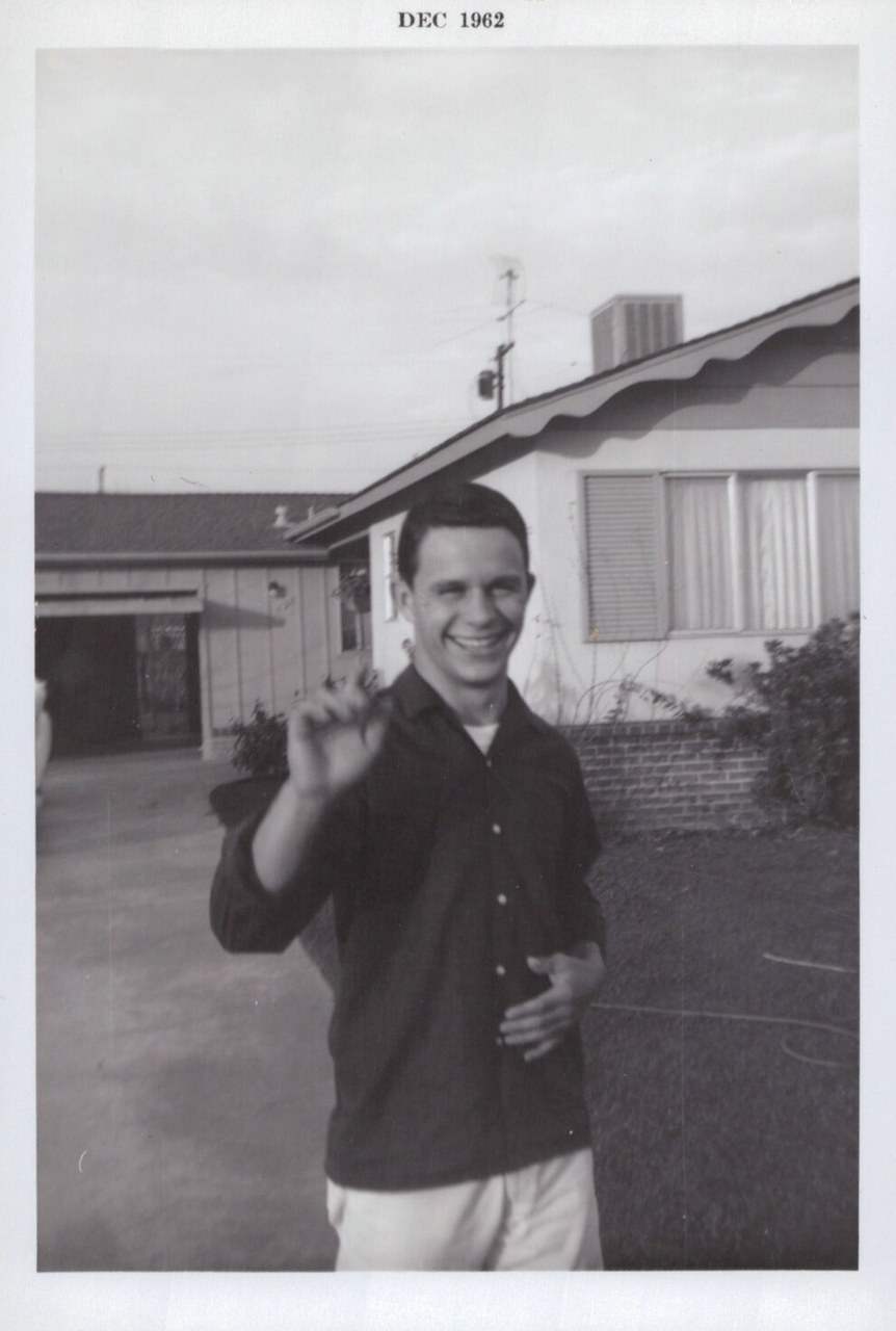 Man waving at camera outside suburban house, December 1962