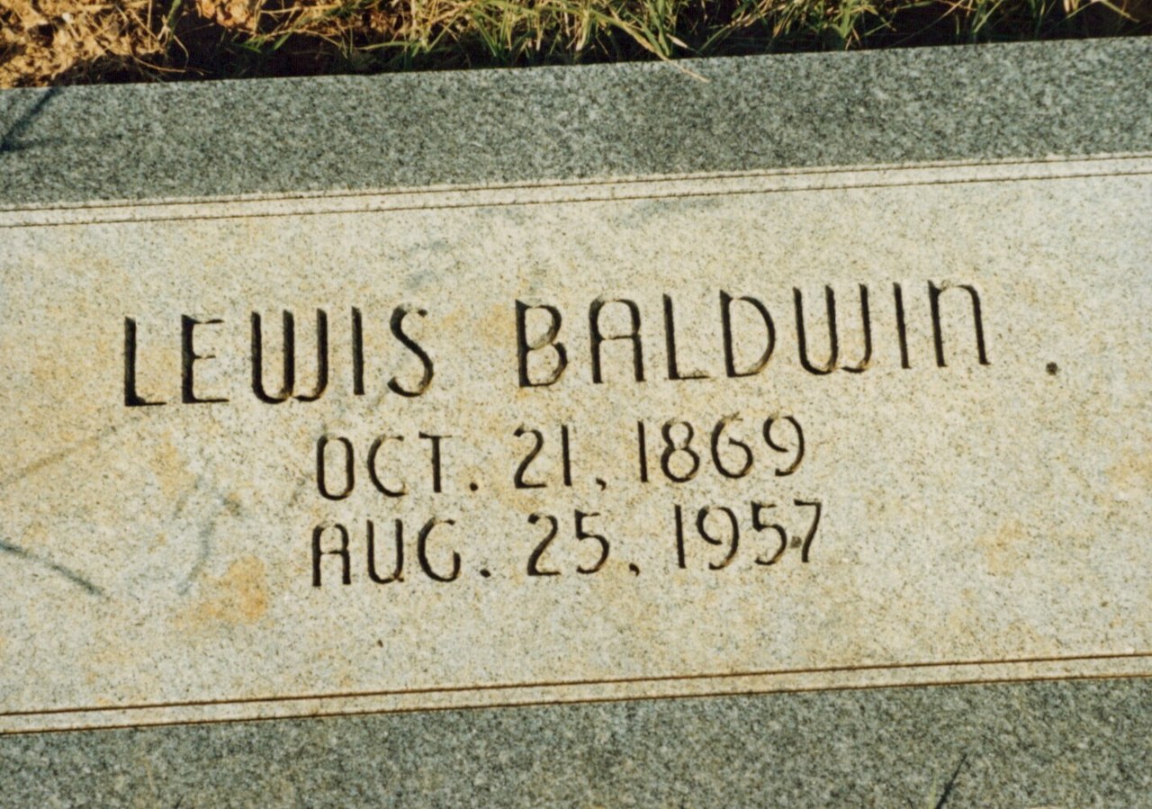 Close-up of a flat granite grave marker inscribed "LEWIS BALDWIN OCT. 21. 1869 AUG. 25. 1957," set at ground level in a cemetery