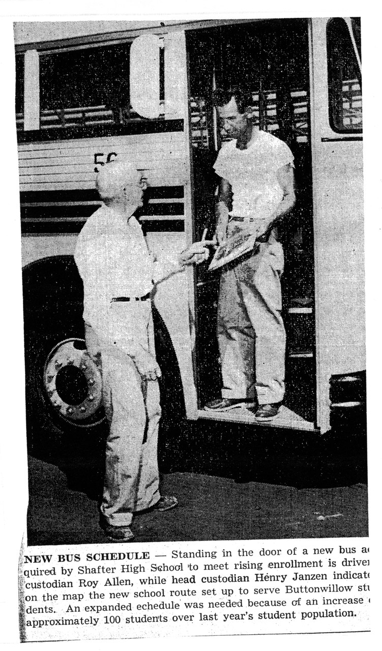 Two men standing in the doorway of a school bus, black-and-white newspaper photo