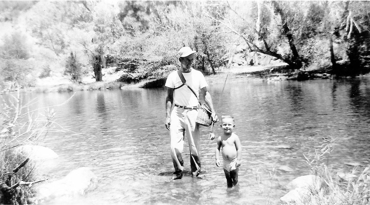 Adult and child wading in a stream while fishing.