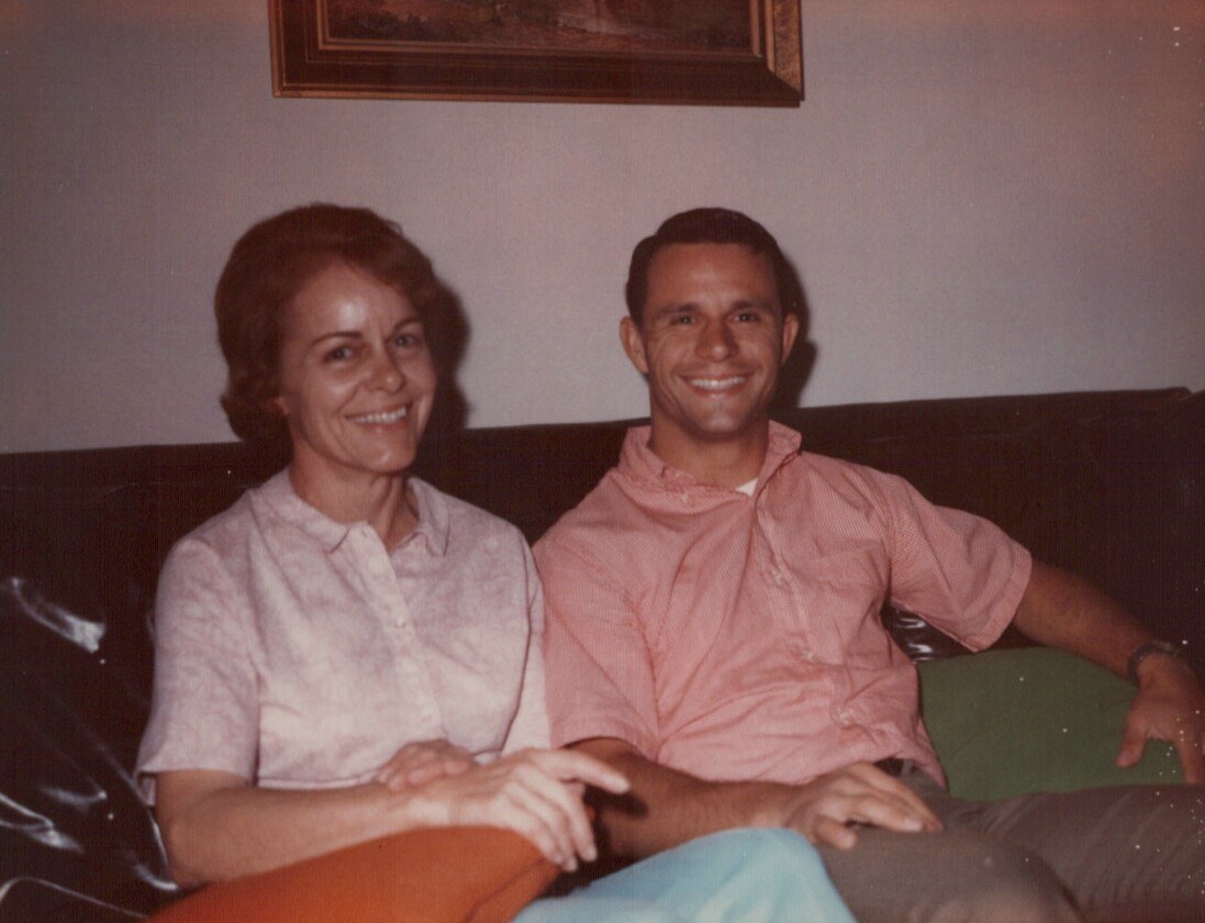 Two people sitting on a dark couch, both smiling at the camera.