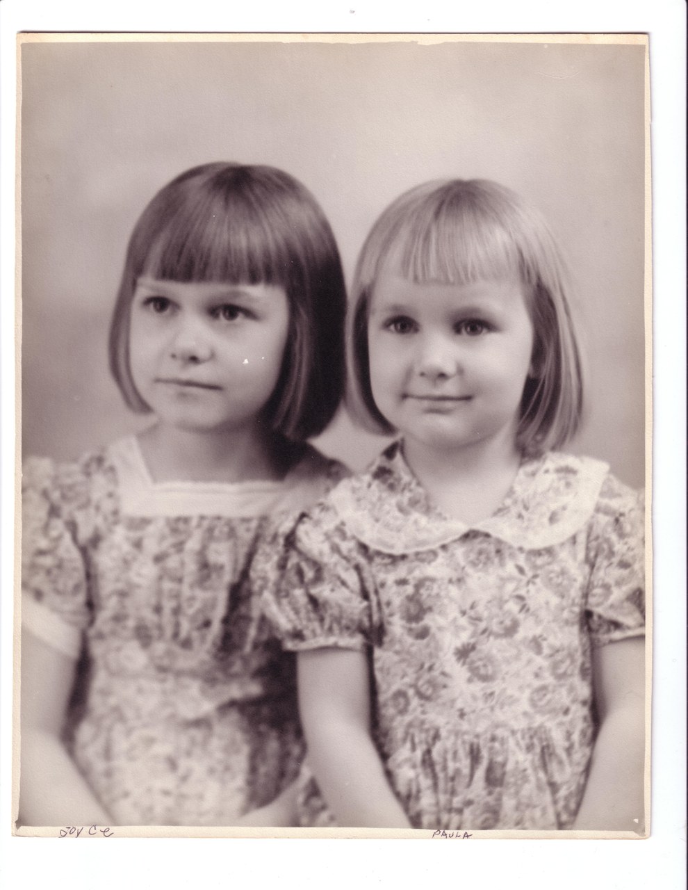 Two young girls with bob haircuts wearing patterned print dresses, formal studio portrait